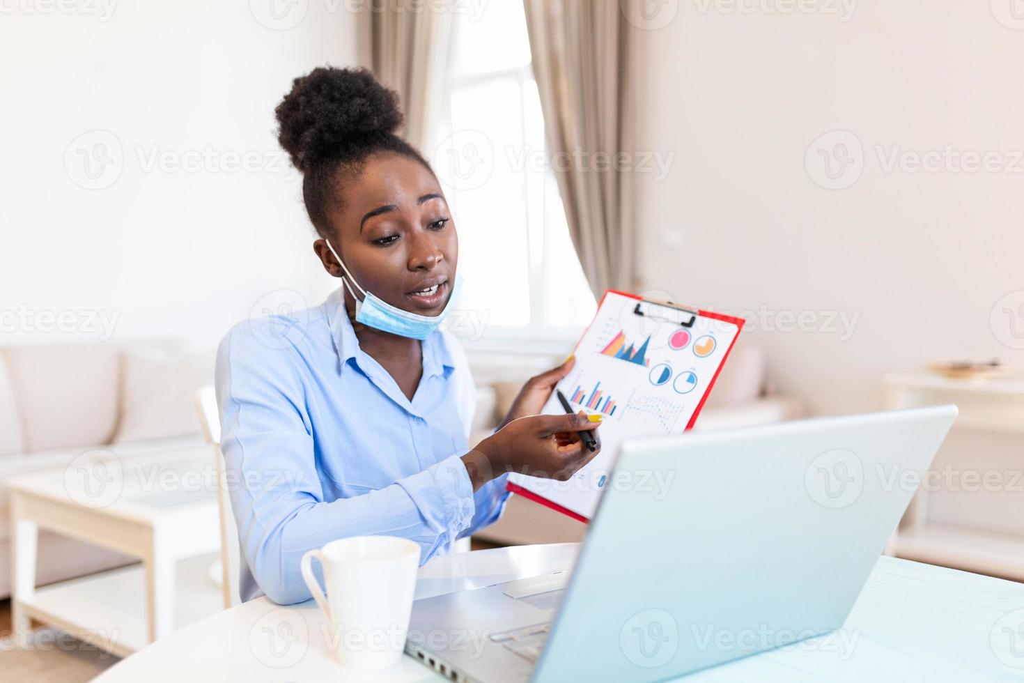 African american businesswoman having video conference while in quarantine during COVID-19 pandemic. Analyzing stock market chart and key performance indicators via video call photo