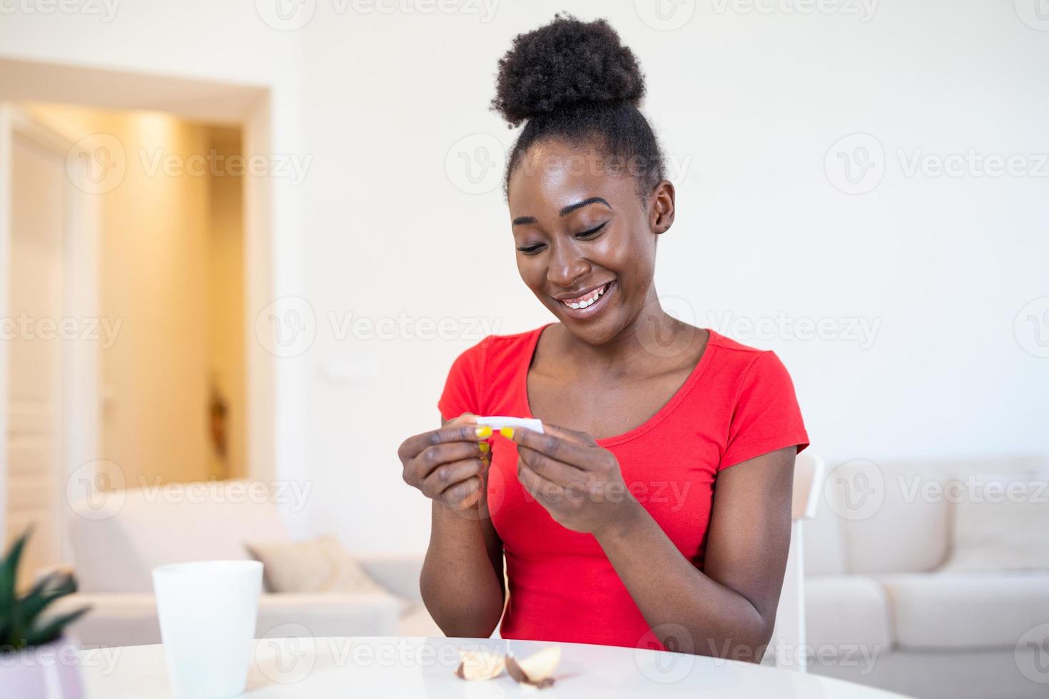 Young african american woman is reading a message from Fortune cookies, does the paper inside of the cookies tell you good things or photo