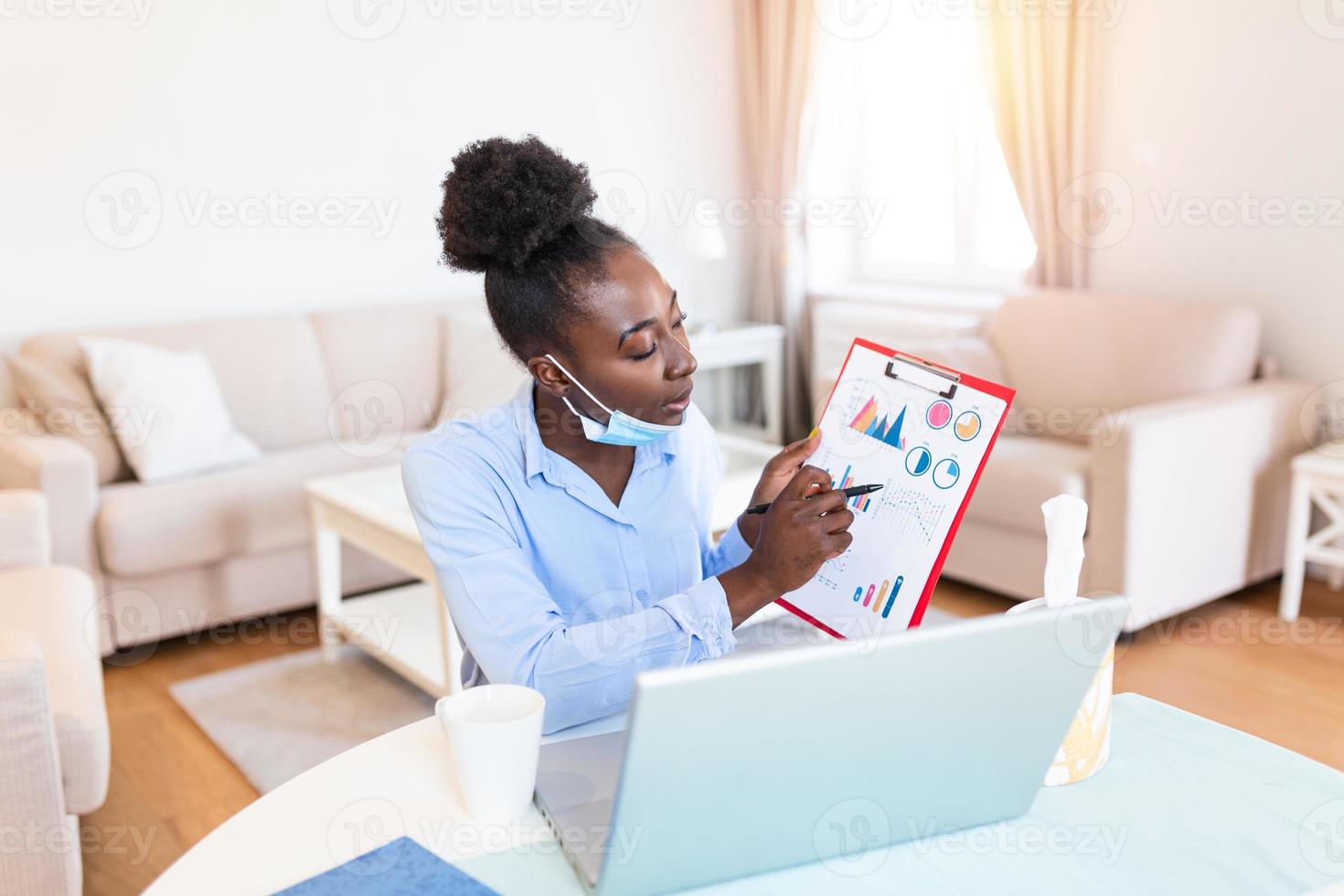 African american businesswoman having video conference while in quarantine during COVID-19 pandemic. Analyzing stock market chart and key performance indicators via video call photo