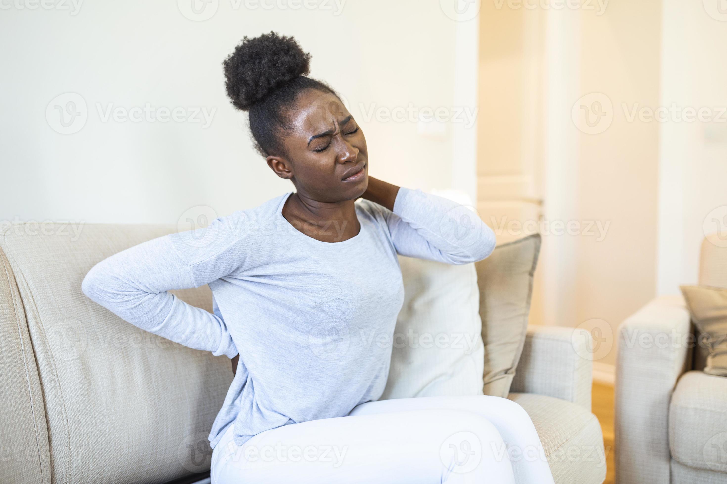 Hurt african American young woman sitting on sofa touching back