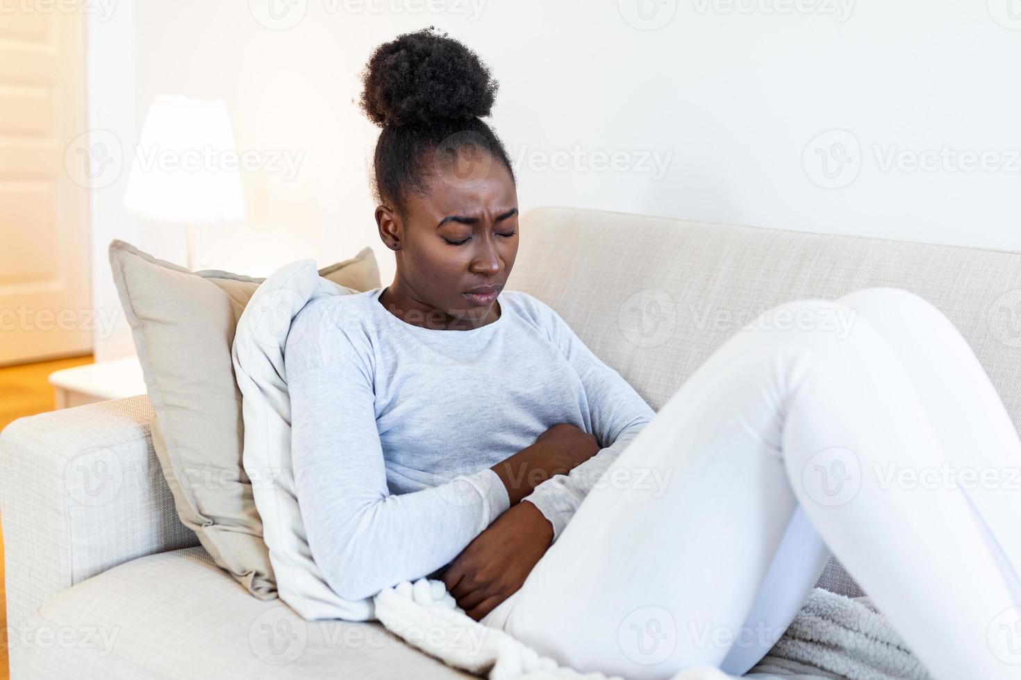 Woman lying on sofa looking sick in the living room. Beautiful young woman lying on bed and holding hands on her stomach. Woman having painful stomachache on bed, Menstrual period photo