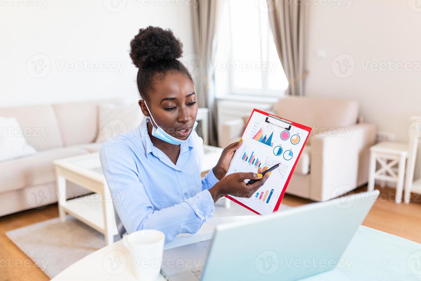 African american businesswoman having video conference while in quarantine during COVID-19 pandemic. Analyzing stock market chart and key performance indicators via video call photo