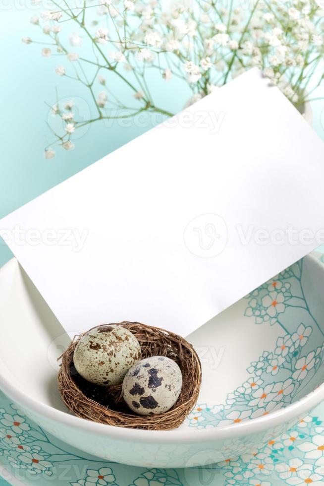 White blank note on plates with floral pattern, quail eggs in nest on light blue Copy space Close up photo