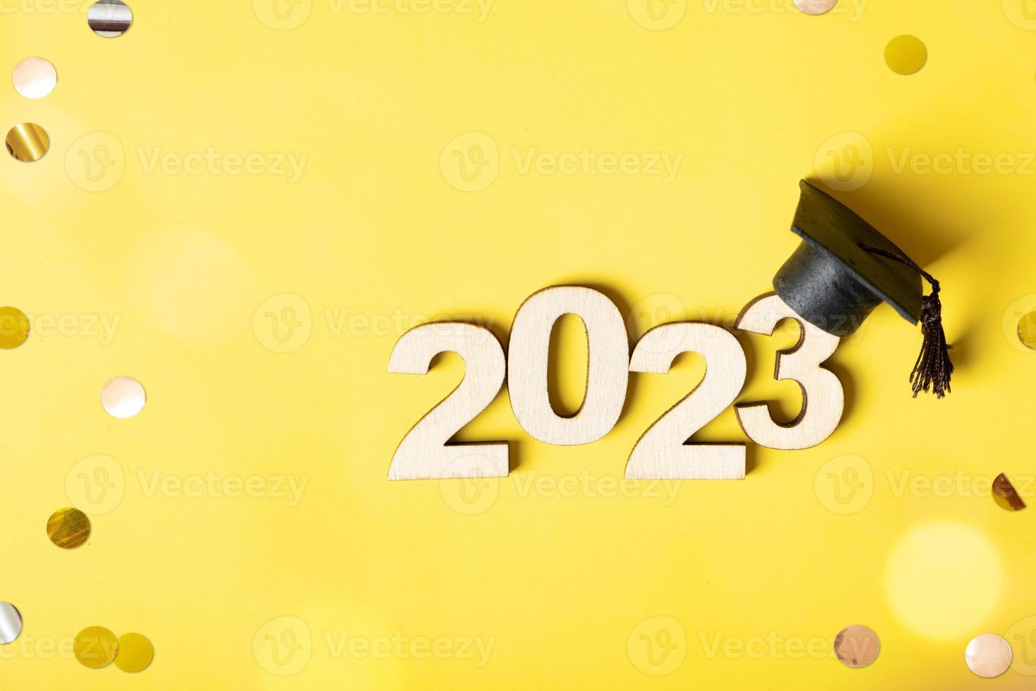 Class of 2023 concept. Wooden number 2023 with graduated cap on colored background with tinsel and bokeh photo