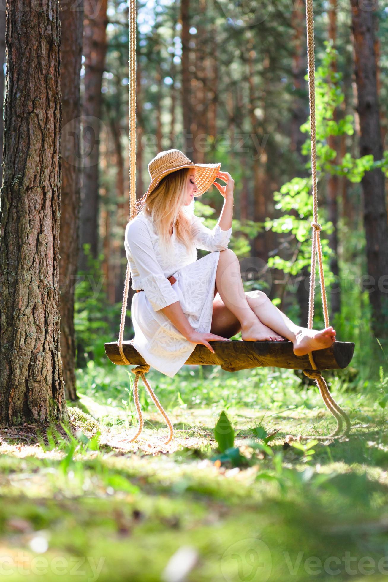https://static.vecteezy.com/system/resources/previews/020/423/927/large_2x/blond-young-woman-with-slender-naked-legs-in-white-dress-and-straw-hat-sitting-on-a-rope-swing-photo.JPG