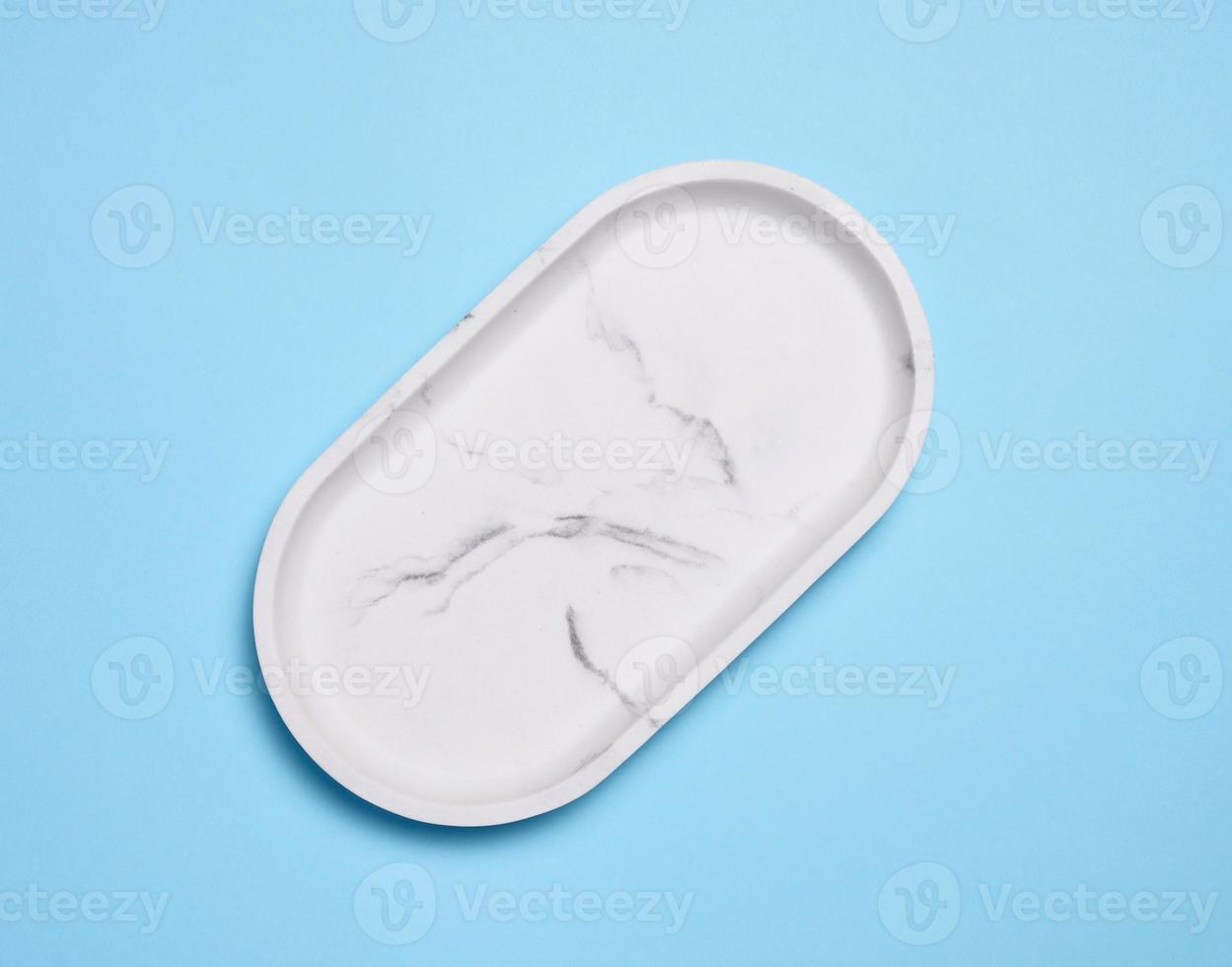 Empty white oval marble plate on a blue background, top view photo