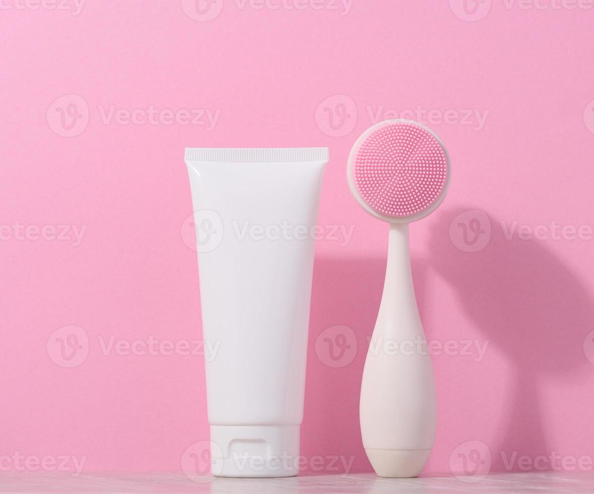 blanco el plastico tubo y un masaje cepillo para facial limpieza en un rosado fondo, artículos para cosmético procedimientos foto