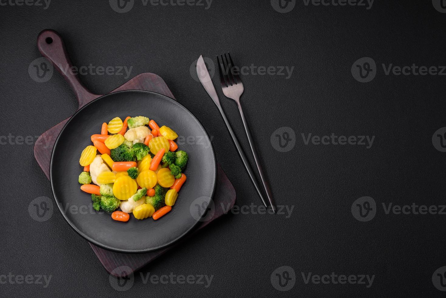 Delicious fresh vegetables steamed carrots, broccoli, cauliflower on a black plate photo