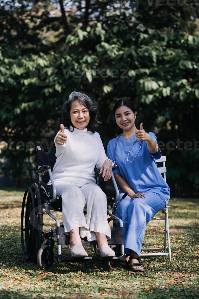 Asian young caregiver nurse support senior older male walking outdoors. Specialist girl doctor help and take care of elderly mature man patient doing physical therapy in public park at nursing home. photo