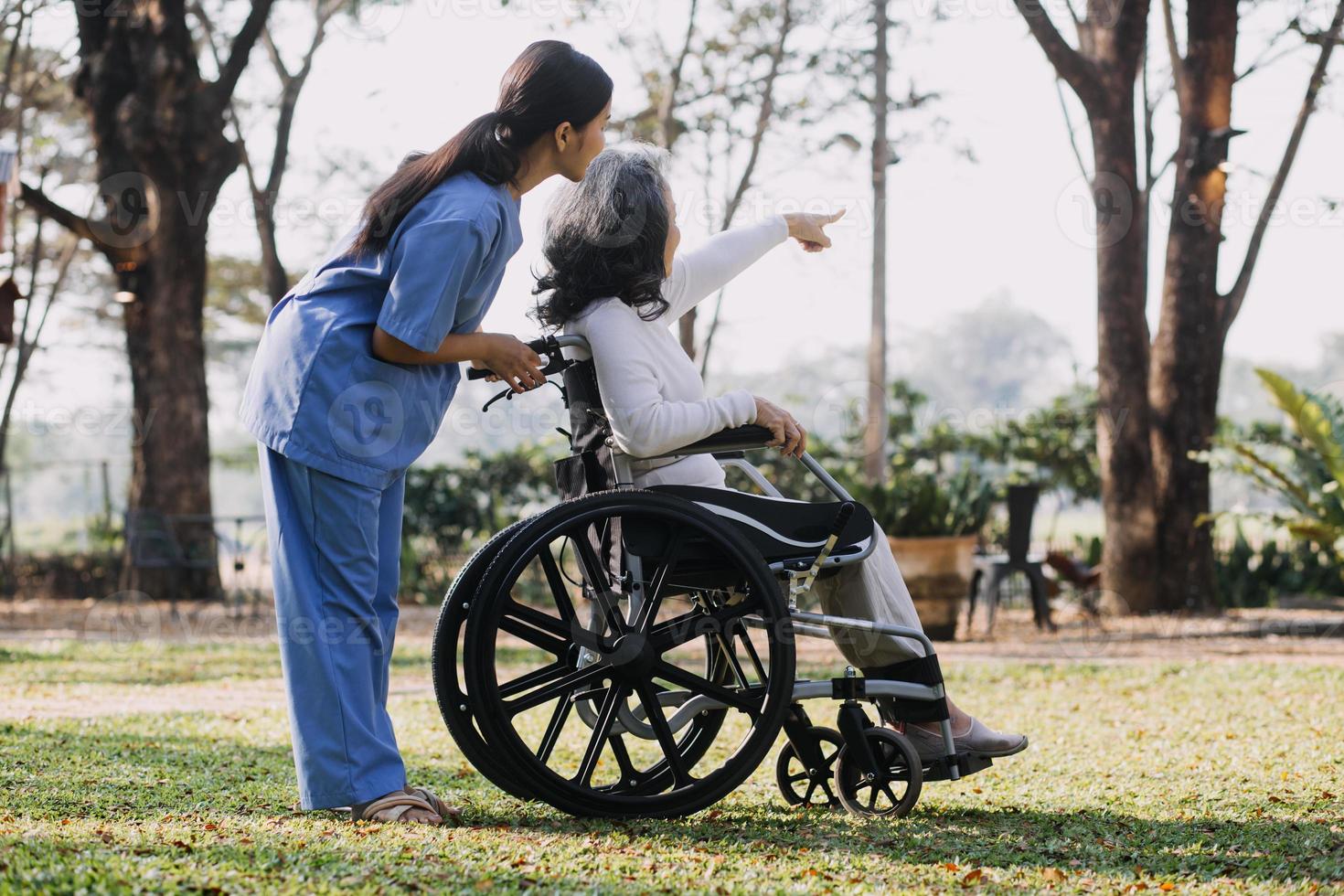 Asian young caregiver nurse support senior older male walking outdoors. Specialist girl doctor help and take care of elderly mature man patient doing physical therapy in public park at nursing home. photo