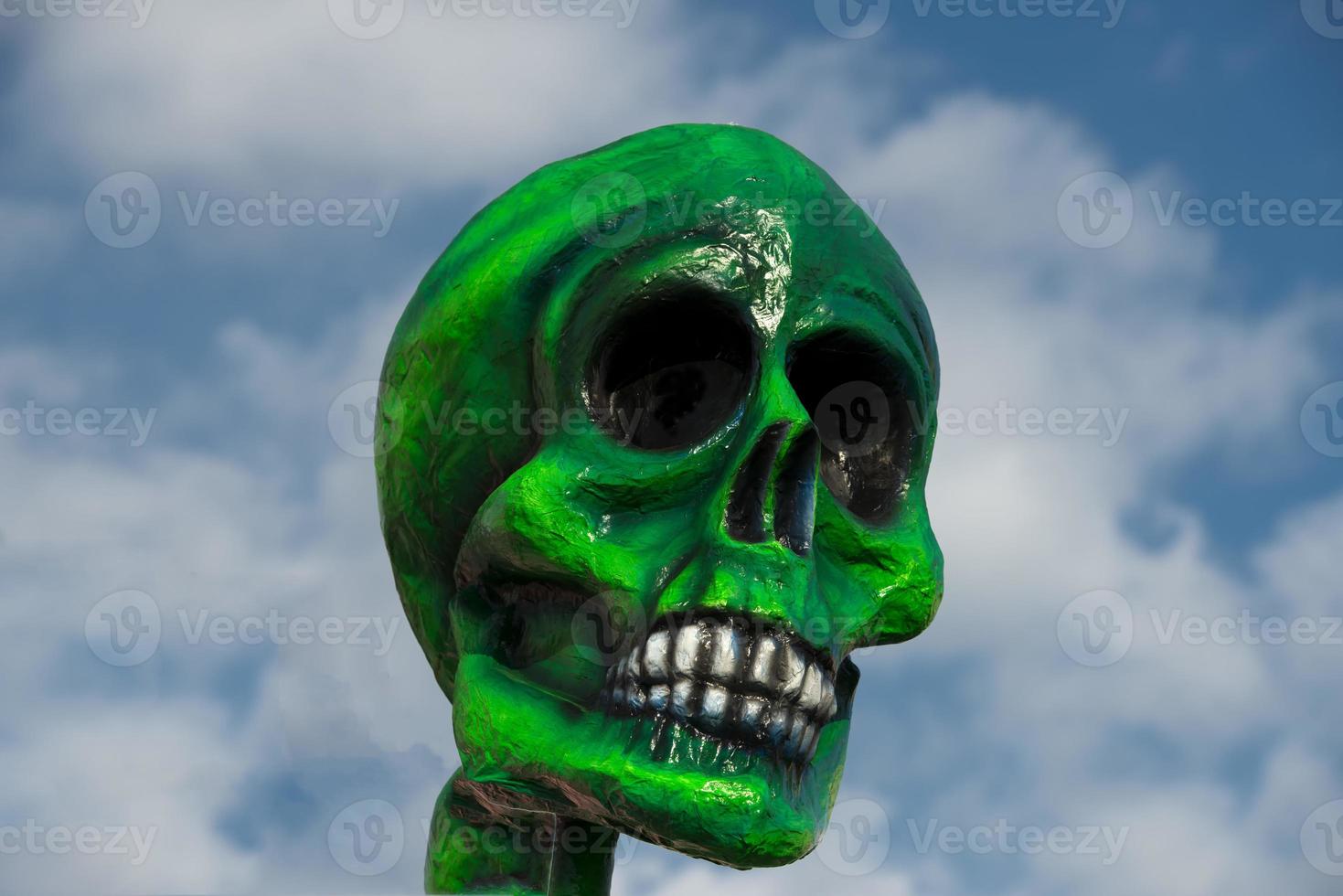 A green paper skull on cloudy sky background photo
