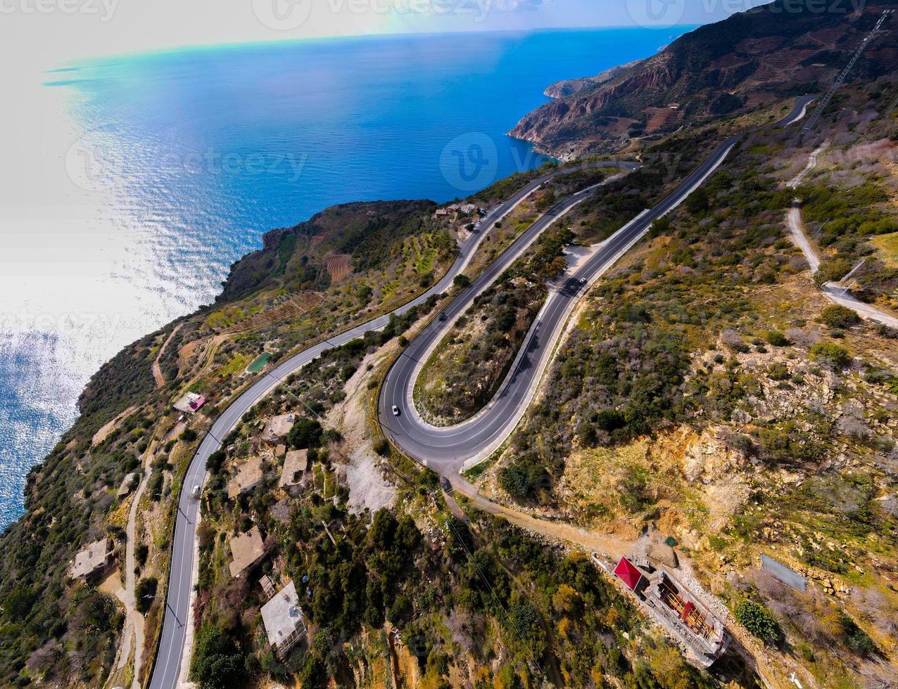 aerial shot of cars passing through a spiral road surrounded by trees in the countryside photo