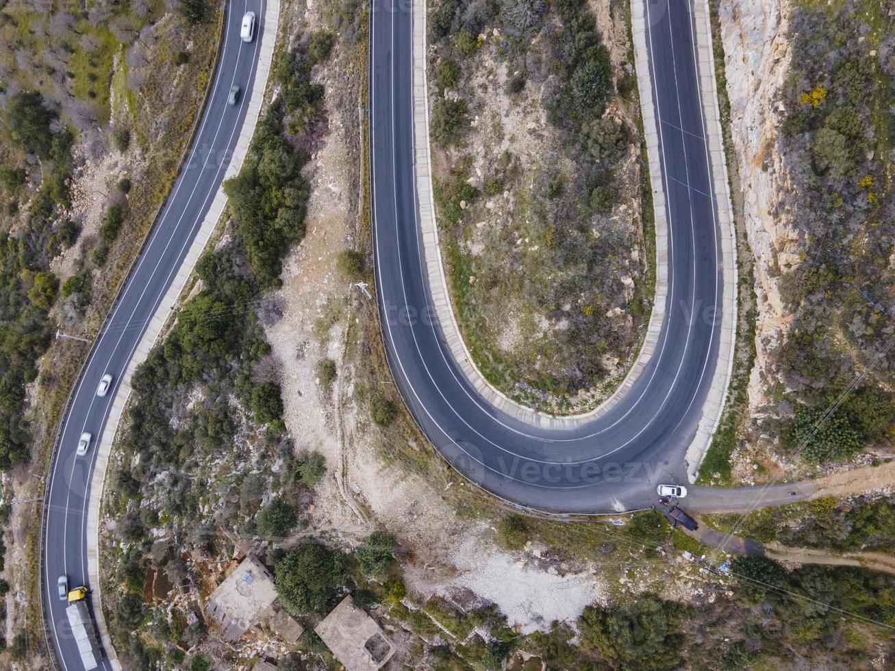 aerial shot of cars passing through a spiral road surrounded by trees in the countryside photo