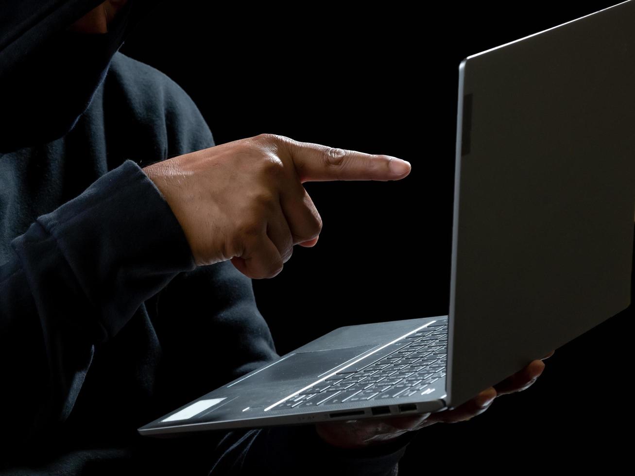 Computer and hands of a man wearing a black shirt, sitting on a chair and a table, is a thief, holding money, counting the amount obtained from hijacking or robbing, in a pitch-black room. photo