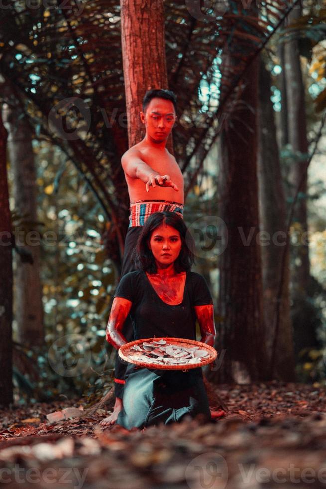 an Asian woman and man were standing in front of a tree while hunting an animal in the middle of the forest until they were covered in blood photo