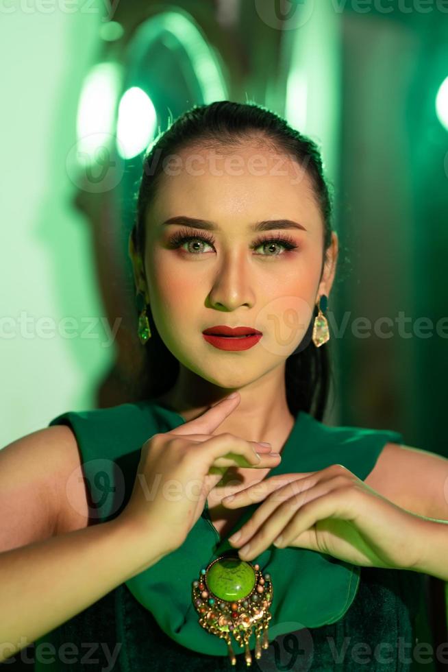 a beautiful Asian woman in a green dress is posing with her hands very gracefully and has green eyes photo