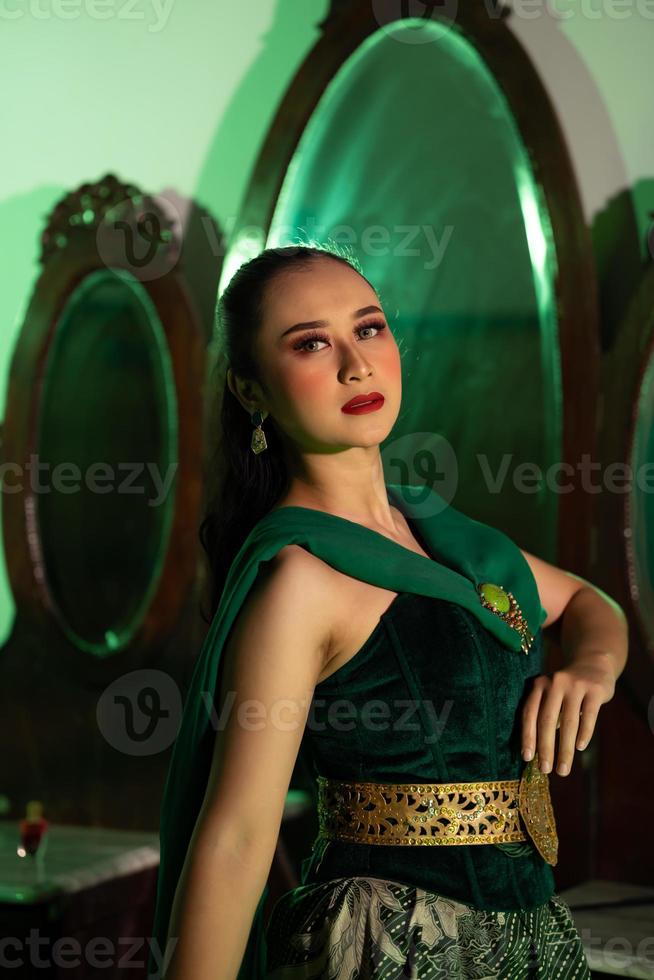 a entertainer woman with a green dress and scarf posing very beautiful and exotic in front of a makeup mirror in a green room photo