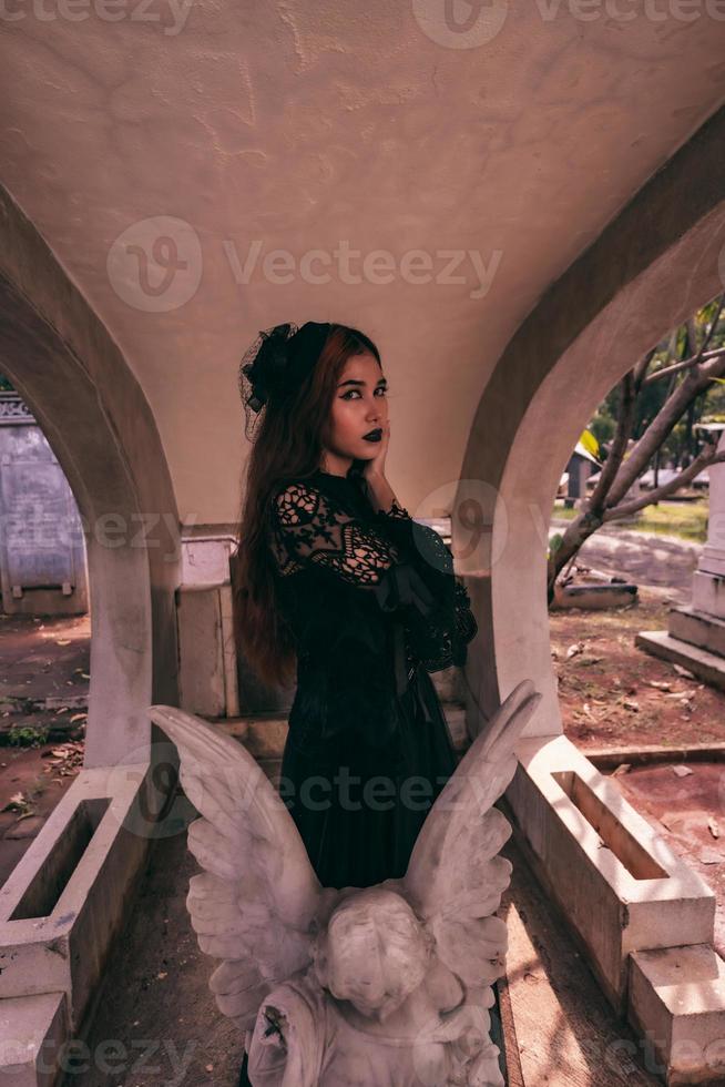 an Asian woman dressed all in black and a scary face was standing over the cemetery photo