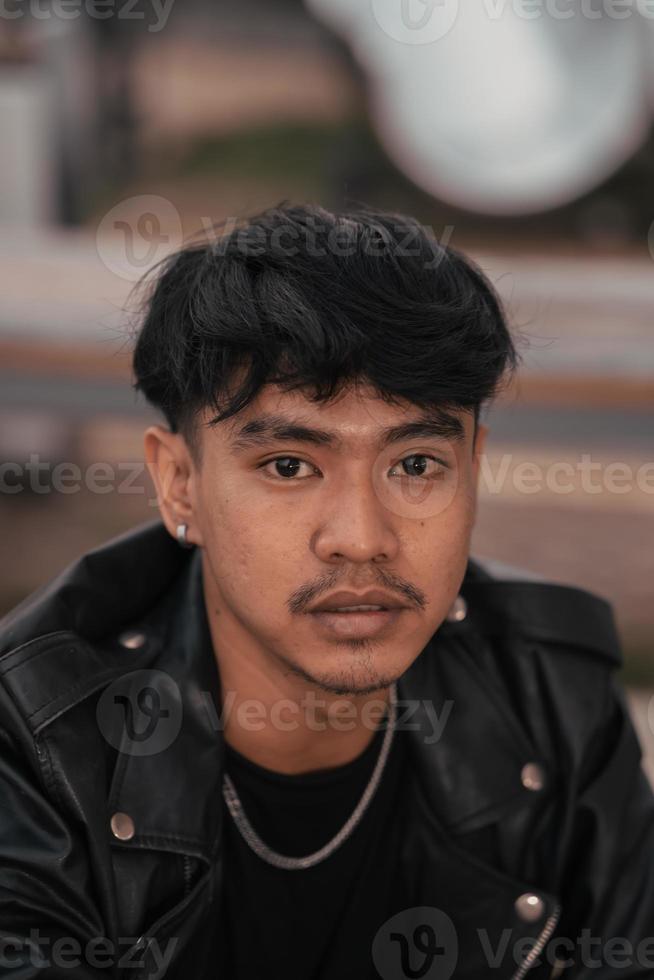 an Asian man with a naughty face wearing a chain necklace and a black leather jacket in a cafe photo