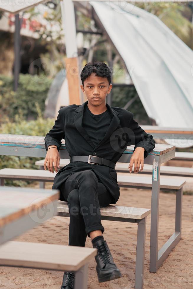 an Asian teenager in a black denim jacket posing by sitting on a cafe chair and relaxing photo