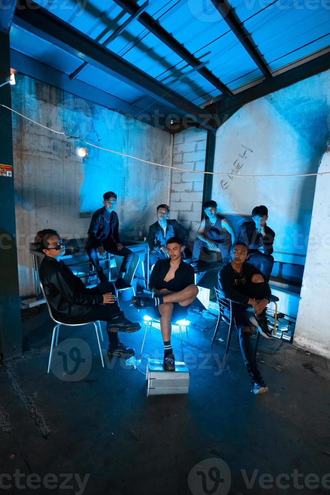 a group of Asian teenagers in black clothes sitting together in a black building with a blue light on the room photo