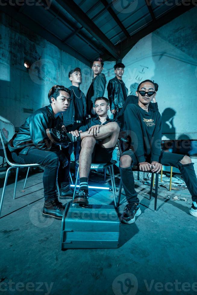 a group of Asian teenagers in black clothes posing very coolly while sitting in a warehouse chair which is lit blue photo