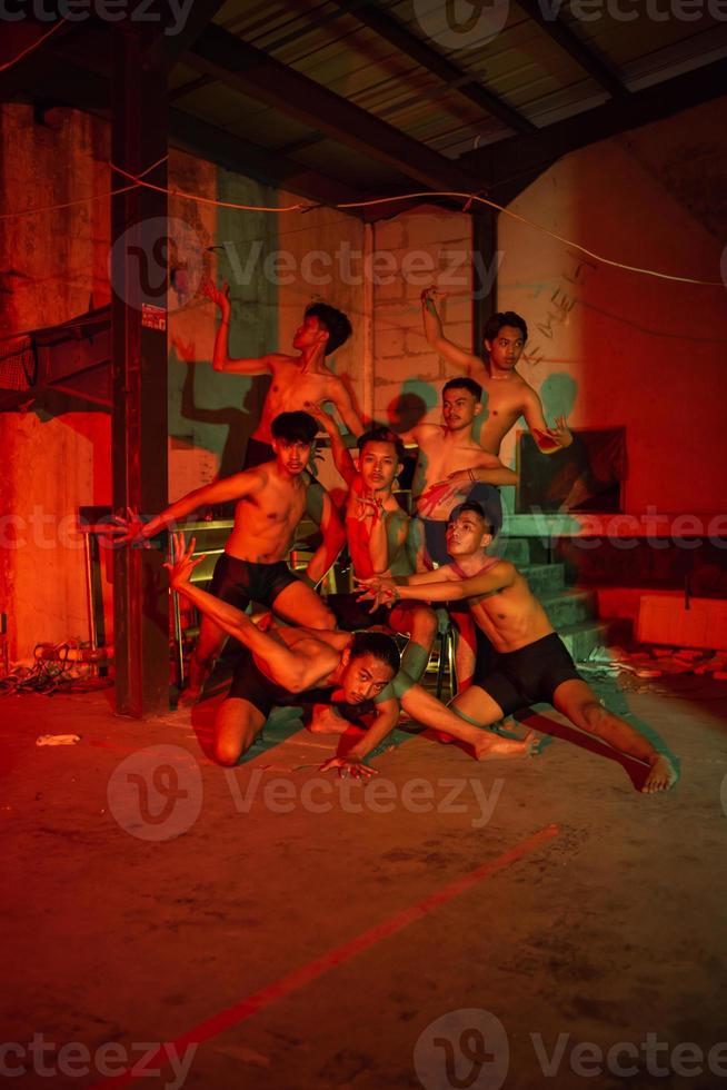 un grupo de hombres sin ropa bailando poses en un antiguo edificio con un rojo ligero foto