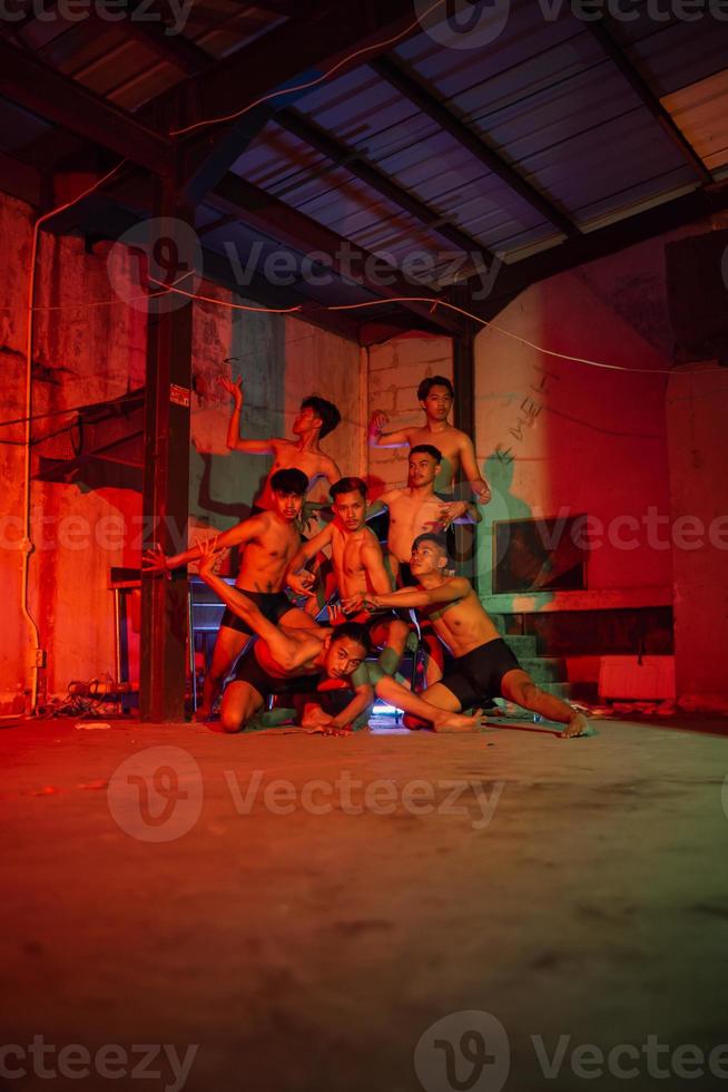 un grupo de hombres sin ropa bailando poses en un antiguo edificio con un rojo ligero foto