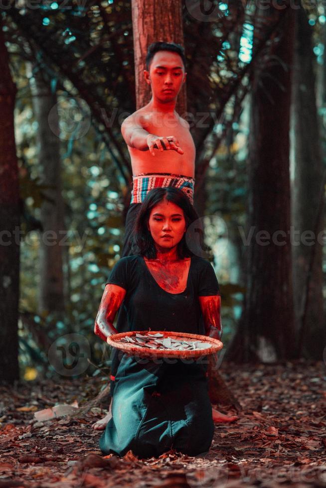 an Asian woman and man were standing in front of a tree while hunting an animal in the middle of the forest until they were covered in blood photo