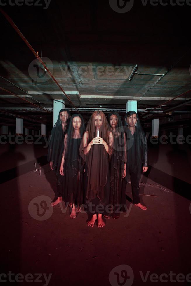 a group of devil worshipers in all black clothes and transparent veils holding candles together during a worship ritual in a building photo