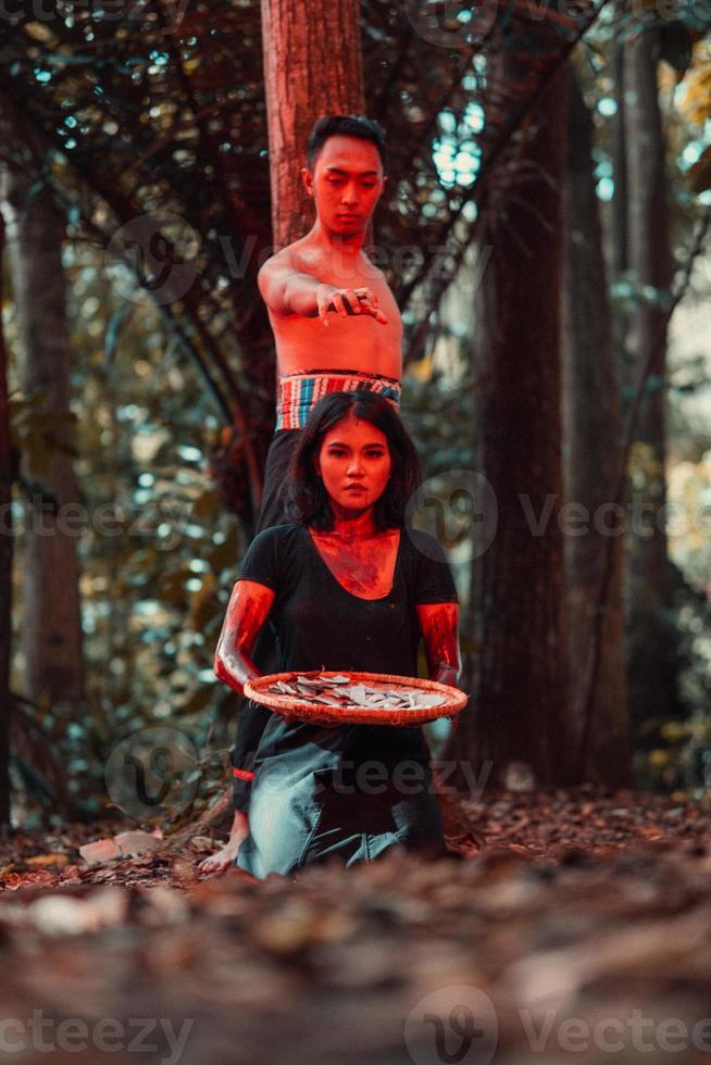 un asiático mujer y hombre fueron en pie en frente de un árbol mientras caza un animal en el medio de el bosque Hasta que ellos fueron cubierto en sangre foto