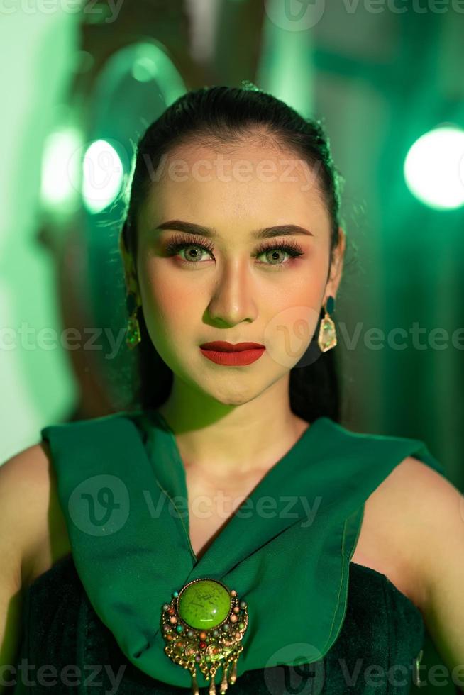 un hermosa asiático mujer en un verde vestir tiene un muy exótico cara con oído y cuerpo joyería mientras foto