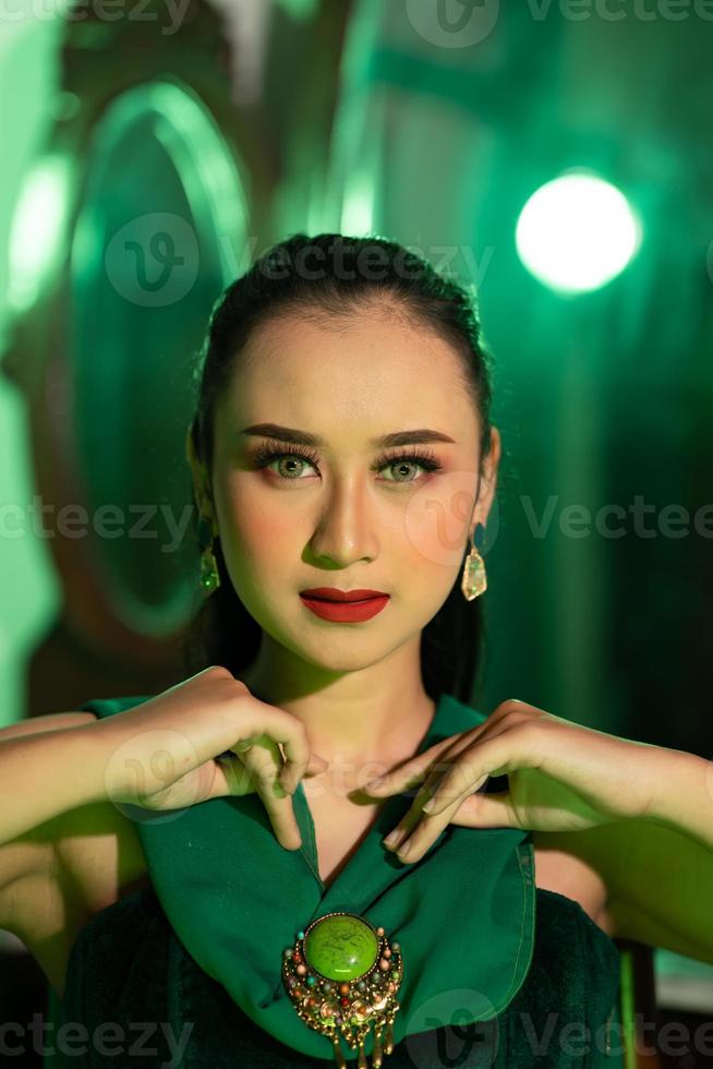 a beautiful Asian woman in a green dress is posing with her hands very gracefully and has green eyes photo