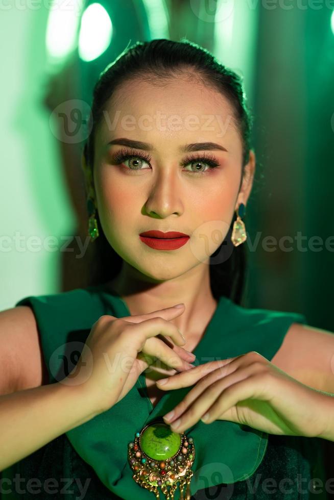 a beautiful Asian woman in a green dress is posing with her hands very gracefully and has green eyes photo