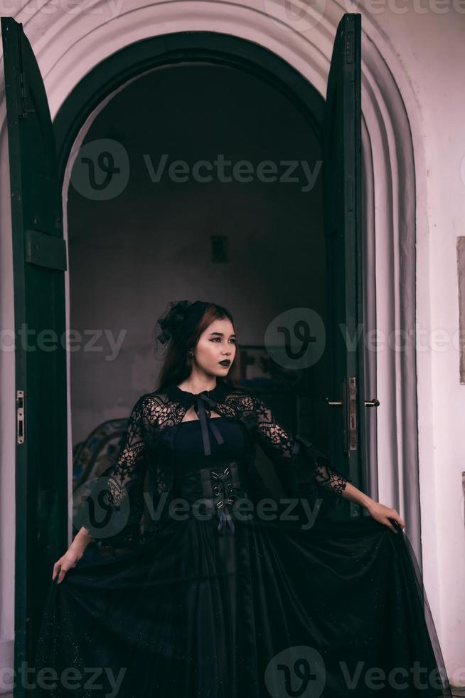 an Asian woman with lips and a black dress standing in front of an open door while visiting a cemetery photo