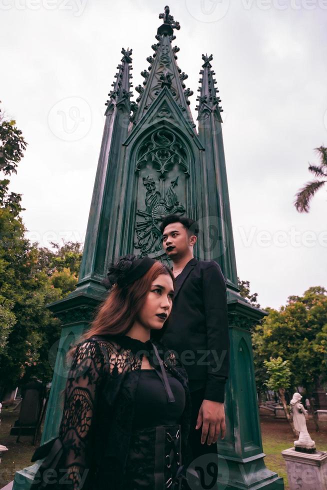 un par de asiático adolescentes en pie en frente de el funeral Monumento y frente a cada otro con todas negro ropa y de miedo expresiones foto