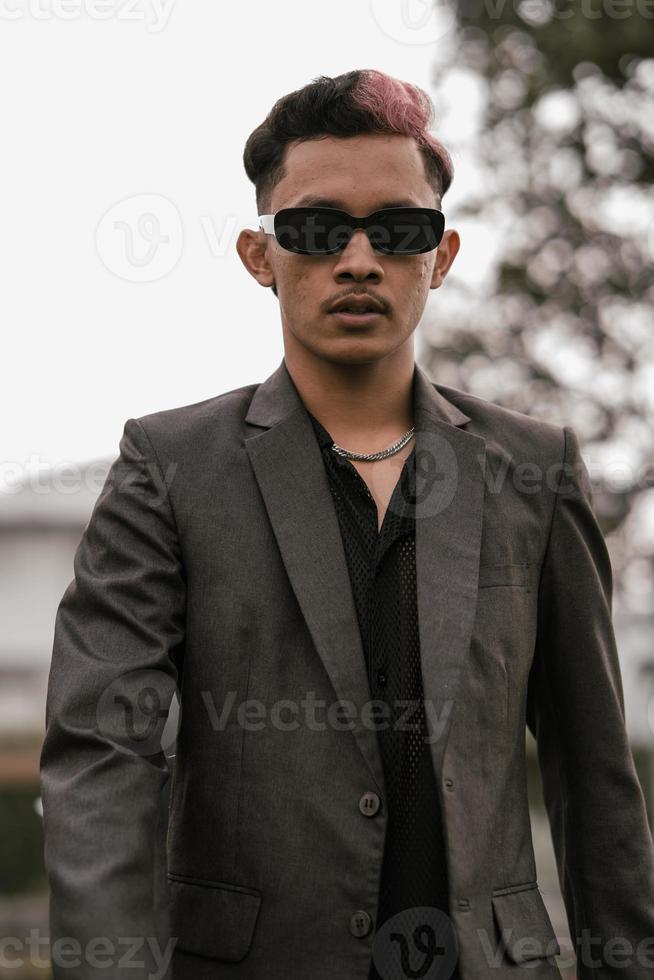 an Asian man with sunglasses posing in a gray suit in the yard photo