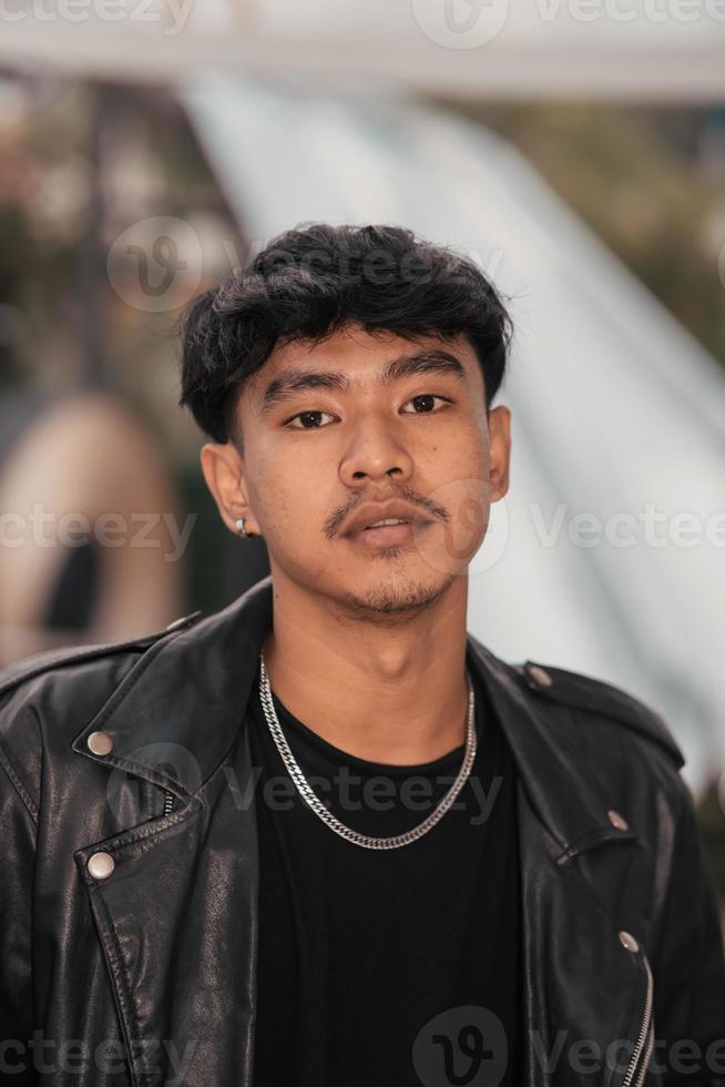 an Asian man with a naughty face wearing a chain necklace and a black leather jacket in a cafe photo