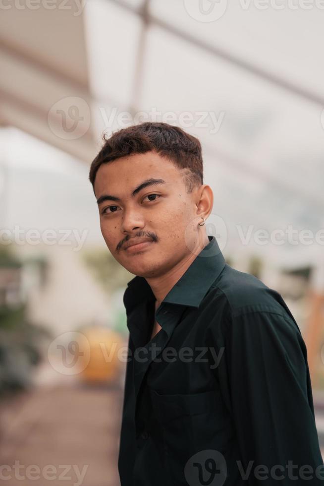 un asiático hombre con un hermoso cara y Bigote vistiendo un negro camisa mientras relajante foto