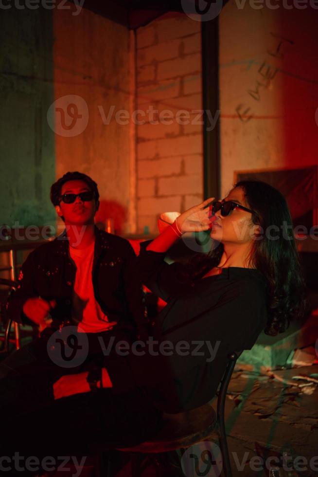 a stylish couple in black clothes are making out in an old barn with colorful lights photo