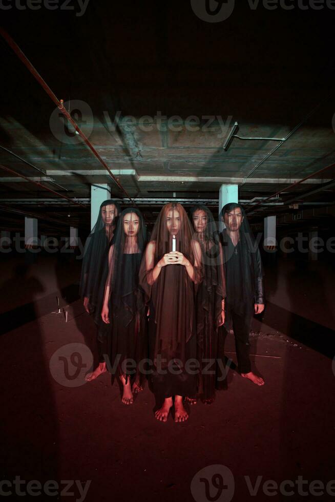 a group of devil worshipers in all black clothes and transparent veils holding candles together during a worship ritual in a building photo