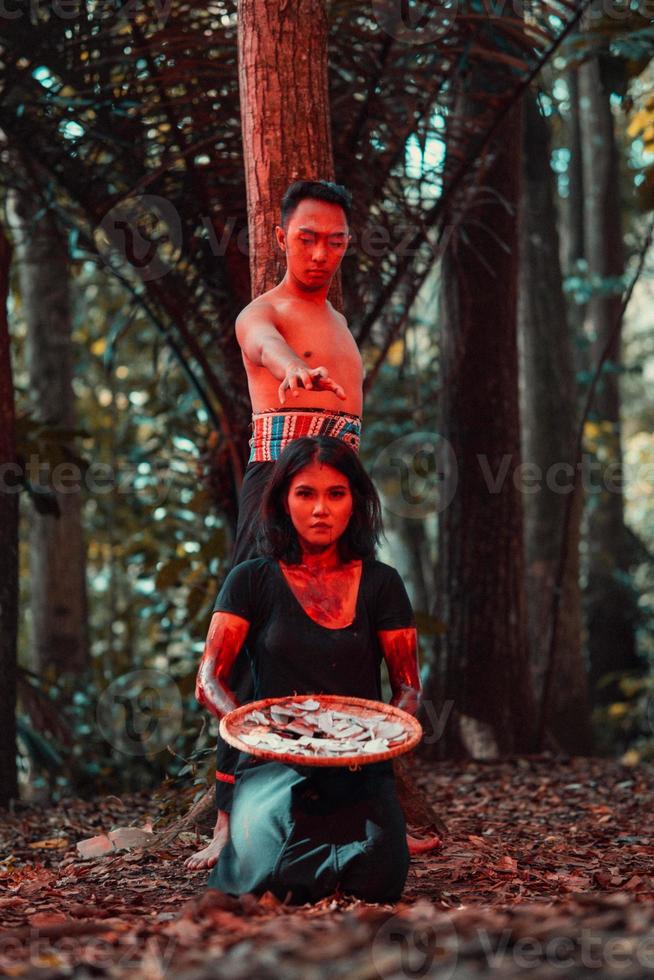 an Asian woman and man were standing in front of a tree while hunting an animal in the middle of the forest until they were covered in blood photo