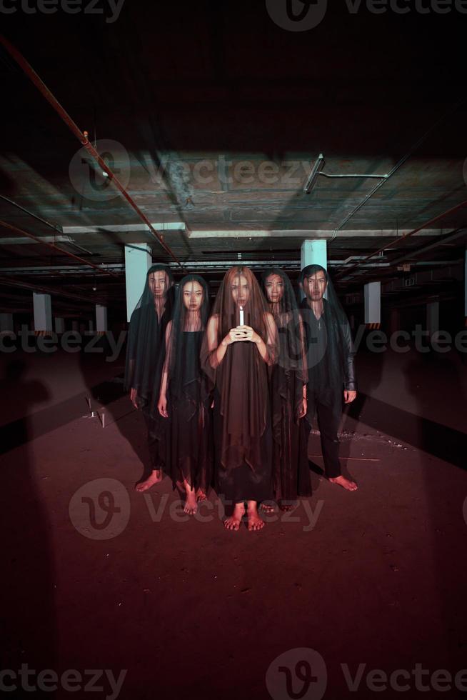 a group of devil worshipers in all black clothes and transparent veils holding candles together during a worship ritual in a building photo