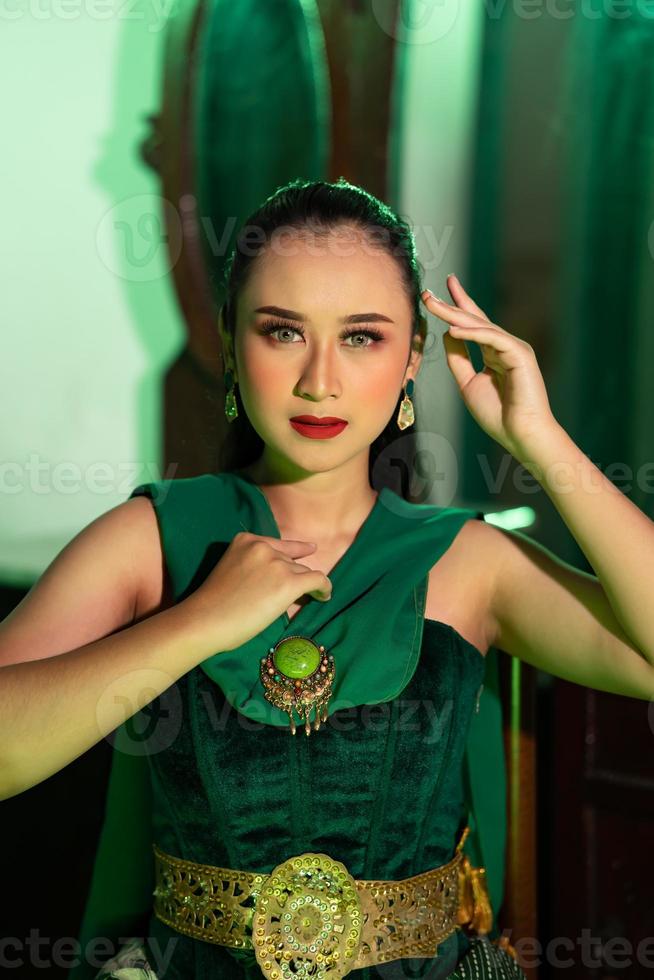 a beautiful Asian woman in a green dress is posing with her hands very gracefully and has green eyes photo