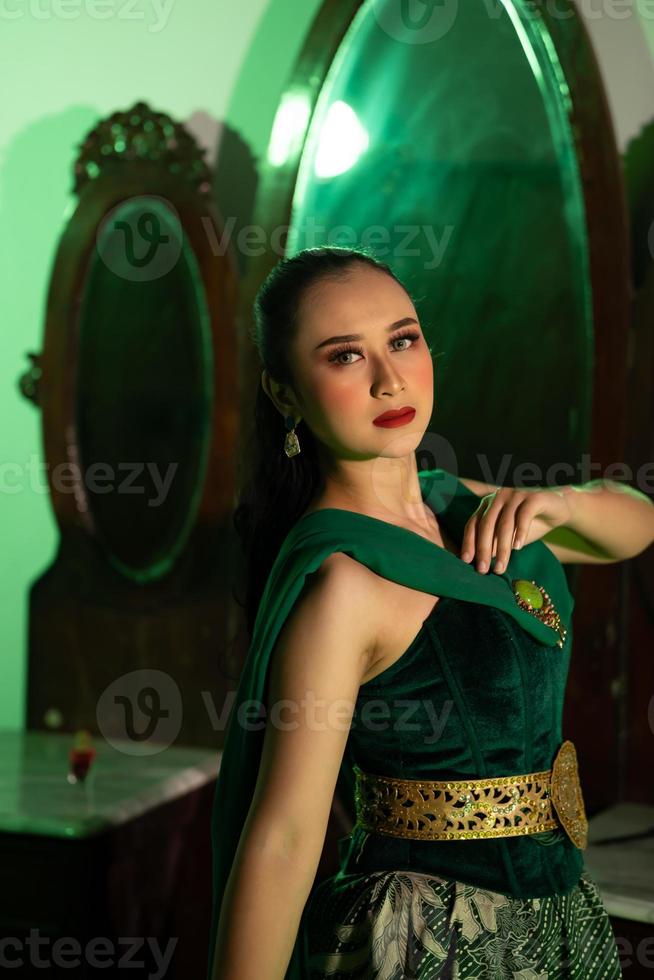 a entertainer woman with a green dress and scarf posing very beautiful and exotic in front of a makeup mirror in a green room photo