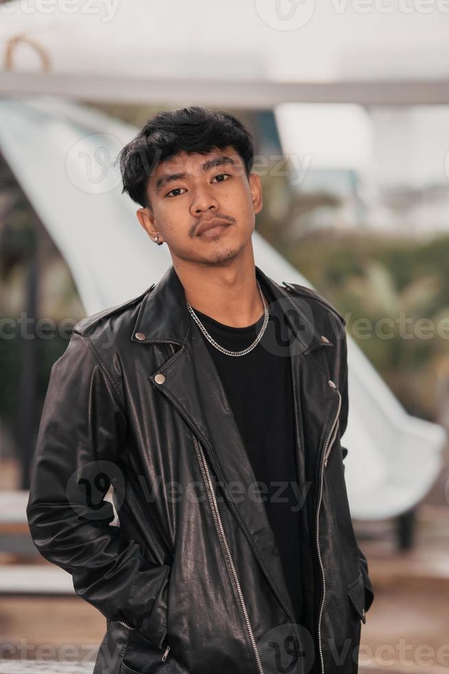 un crecido hombre en un negro cuero traje y cadena collar posando muy gallardamente en el ancho foto