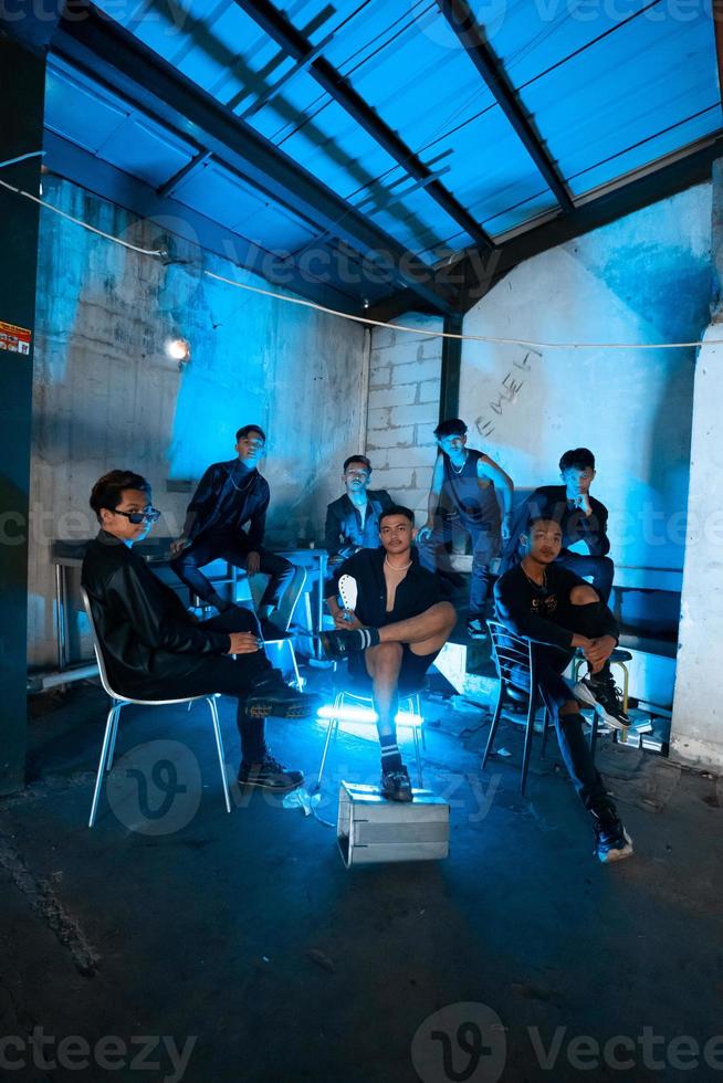 un grupo de asiático adolescentes en negro ropa sentado juntos en un negro edificio con un azul ligero en el habitación foto