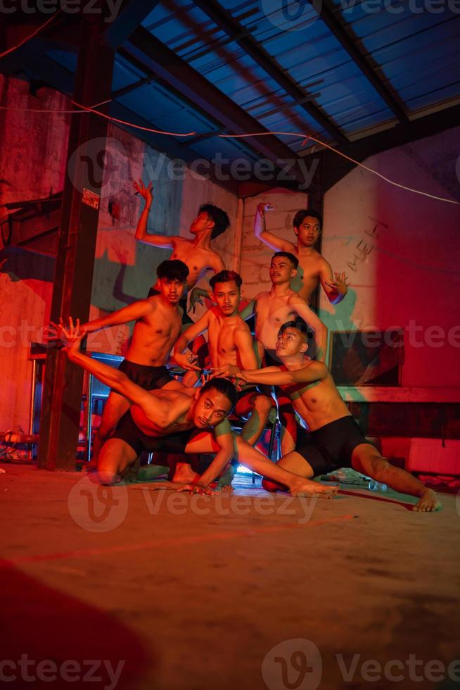 a group of men without clothes dancing poses in an old building with a red light photo