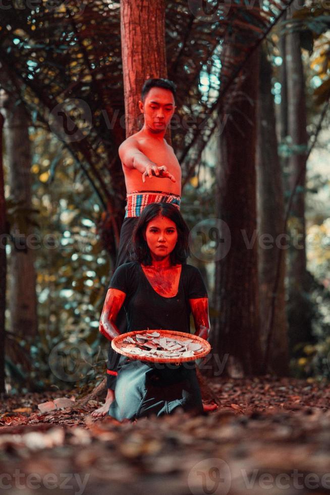 an Asian woman and man were standing in front of a tree while hunting an animal in the middle of the forest until they were covered in blood photo