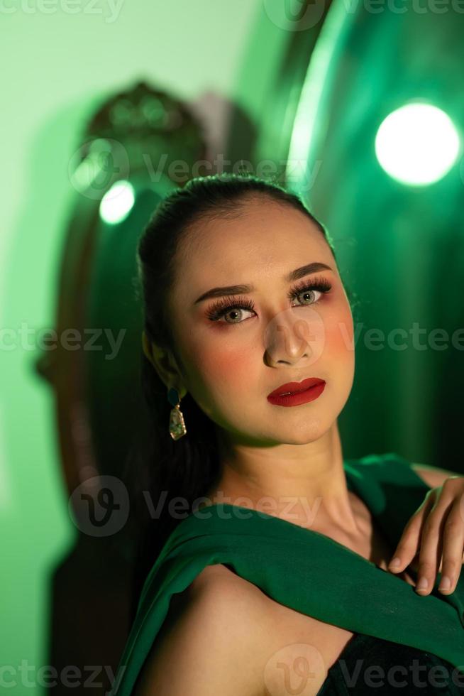 a entertainer woman with a green dress and scarf posing very beautiful and exotic in front of a makeup mirror in a green room photo